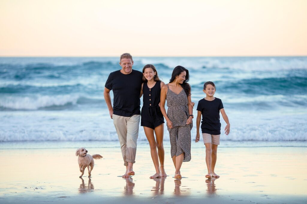 Familia de 4 miembros y perro en la playa sonrientes, para ilustrar artículo de familias perfectas desde una perspectiva psicológica